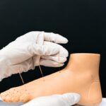 Close-up of hands performing acupuncture on an artificial foot model for educational purposes.
